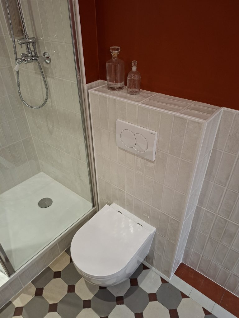 WC suspendus dans salle de bain avec carrelage blanc et gris et cabochons bordeaux