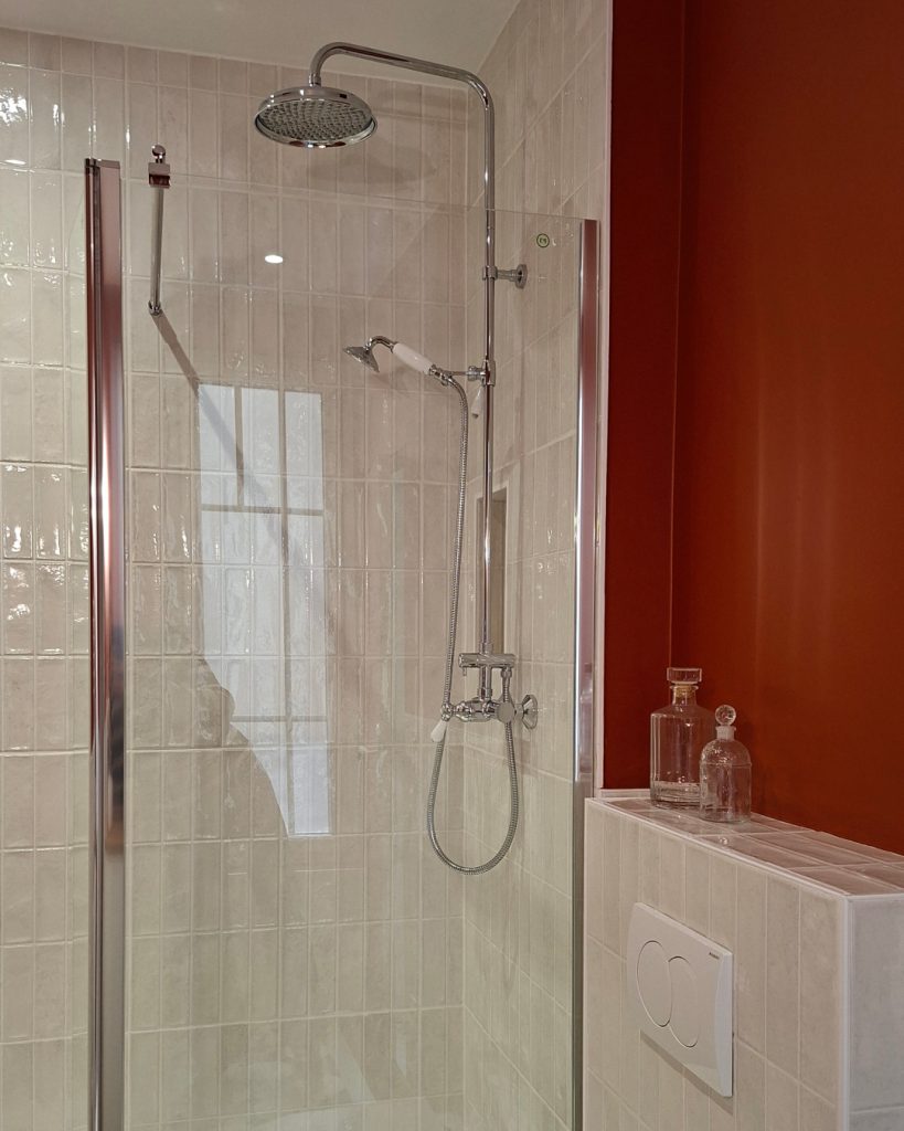 grande douche avec paroi vitrée et robinetterie à l'esprit ancien. zelliges blanc cassé et murs terre battue