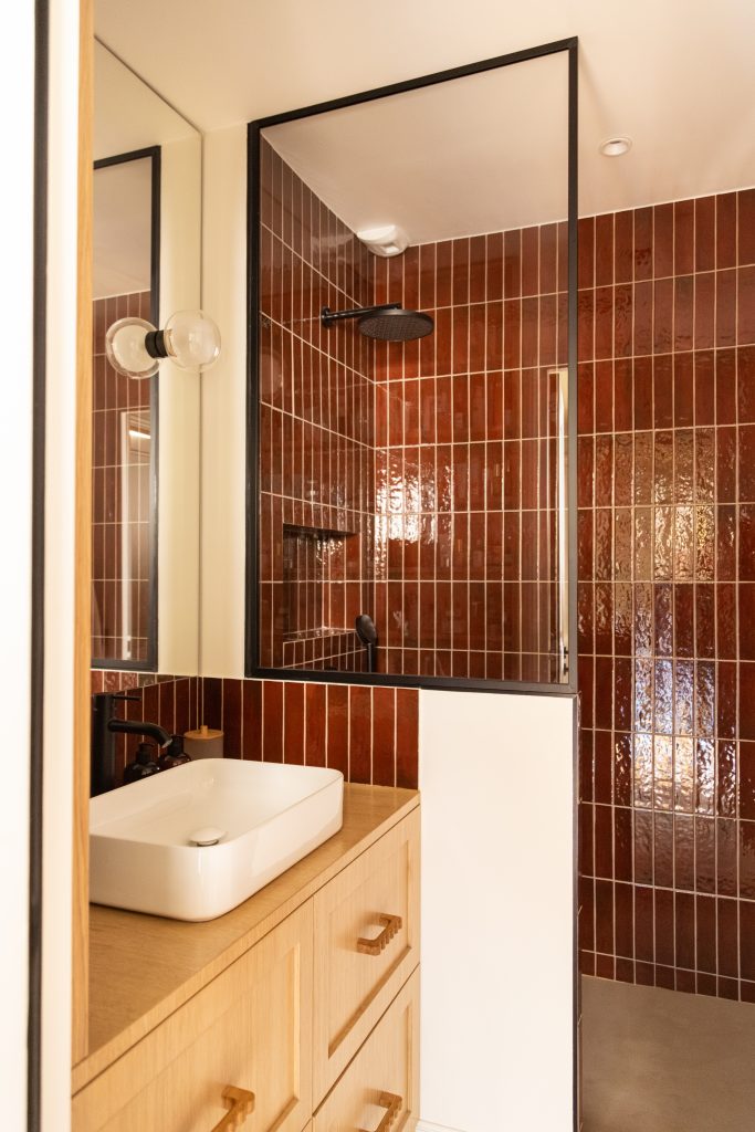 ancien placard transporté en salle d'eau avec douche à l'italienne en zelliges rouge, meuble vasque sur mesure en placage chêne avec robinetterie noire