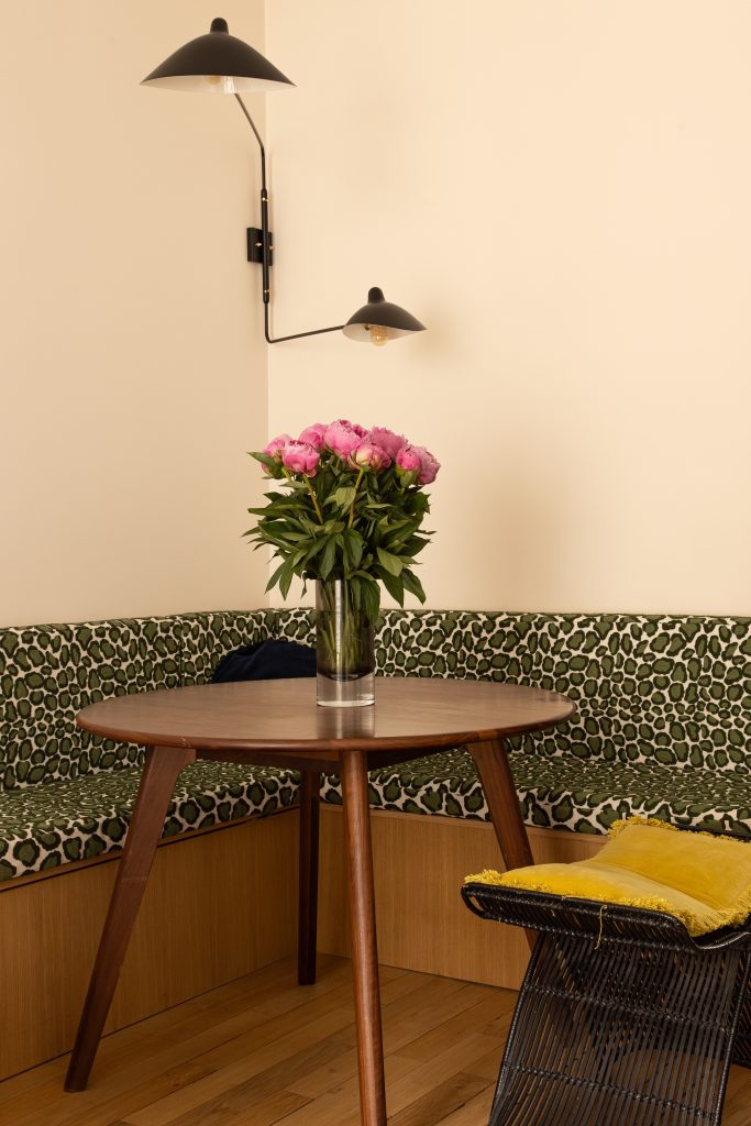 Banquette d'angle en placage chêne avec rangements et coussins léopard vert autour d'une table ronde en noyer et applique murale déportée